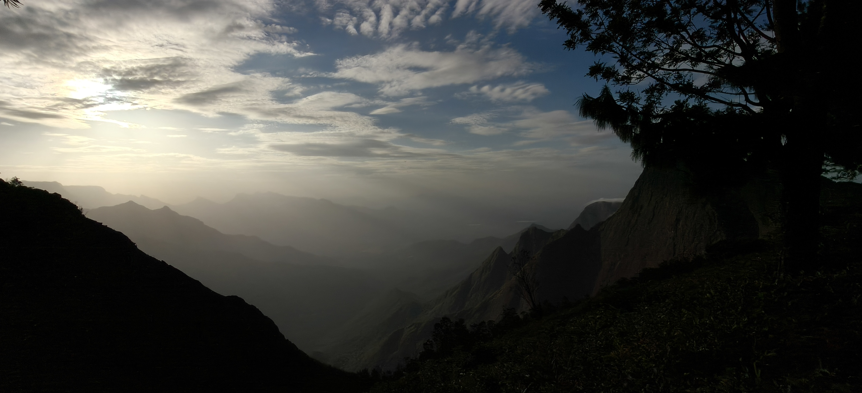 Kolukkumalai valley view with dramatic clouds, soft sunlight and mountain silhouettes